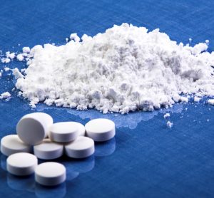 White pills with a small heap of white powder on a blue table - idea of pharmaceutical ingredients