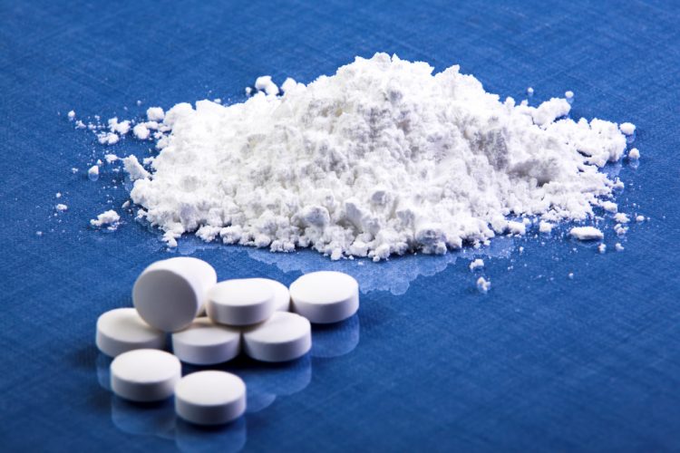 White pills with a small heap of white powder on a blue table - idea of pharmaceutical ingredients