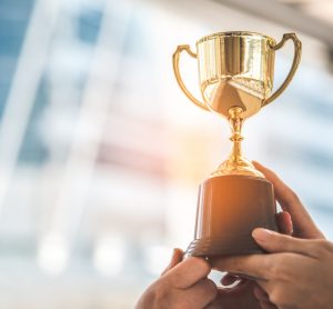 Close up of several people's hands raising a gold trophy - idea of an award