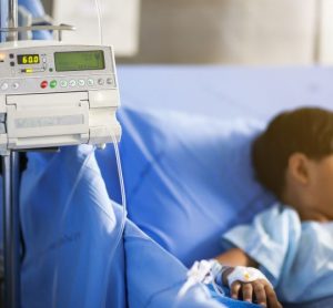 Little boy in a hospital bed being fed intravenous fluids by an infusion pump