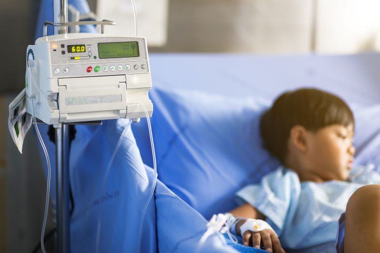 Little boy in a hospital bed being fed intravenous fluids by an infusion pump