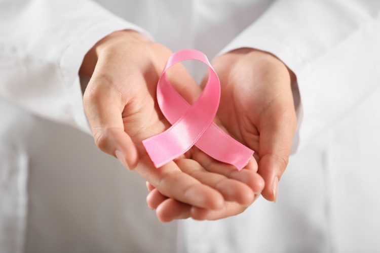 Doctor in white coat holding pink ribbon - symbol of breast cancer