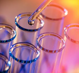 Row of test tubes with a pipette dropping a liquid into one on a red and yellow background