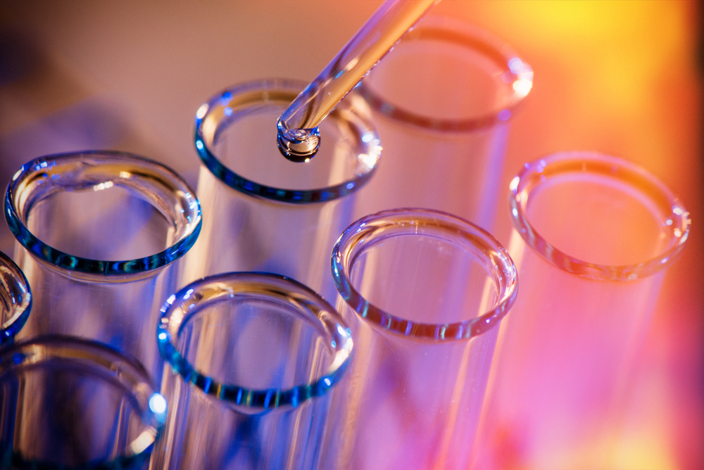 Row of test tubes with a pipette dropping a liquid into one on a red and yellow background