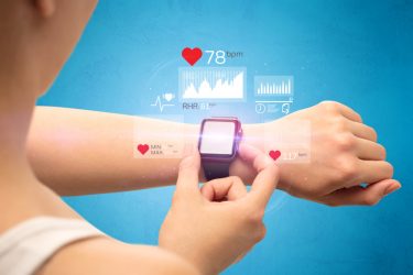 Woman touching the screen of her smart watch - one example of a wearable device to monitor health - to see a heart rate graph