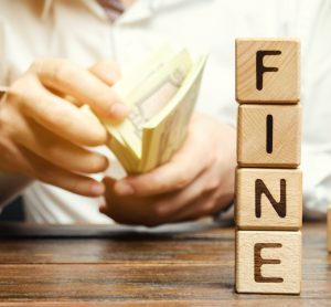 man holding a wad of paper money notes with 'fine' spelt in blocks next to him