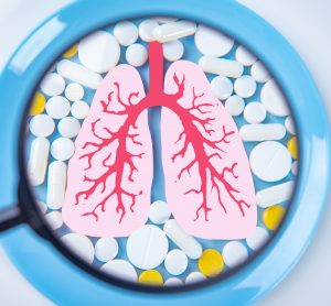 tablets surrounding a diagra of the lungs under a magnifying glass - idea of respiratory drug development/testing