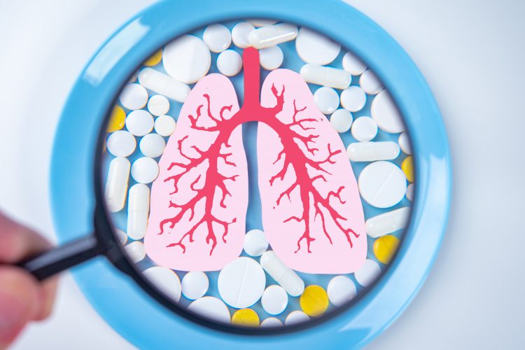 tablets surrounding a diagra of the lungs under a magnifying glass - idea of respiratory drug development/testing