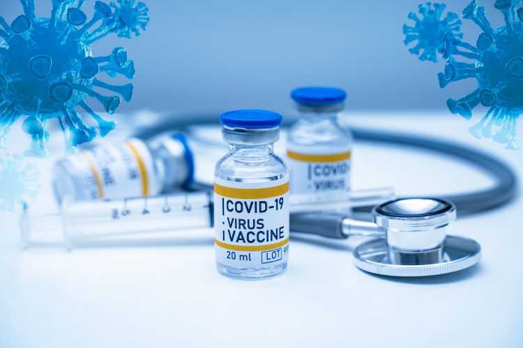 Vials labelled 'COVID-19 Vaccine' next to stethoscope, surrounded by blue cartoon SARS-CoV-2 particles