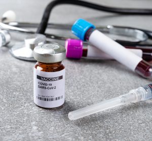 vial labelled 'COVID-19 SARS-CoV-2 VACCINE' next to syringe blood samples in tube and stethoscope