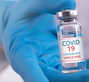 vial in blue gloved hand labelled 'COVID 19 Coronavirus Vaccine'