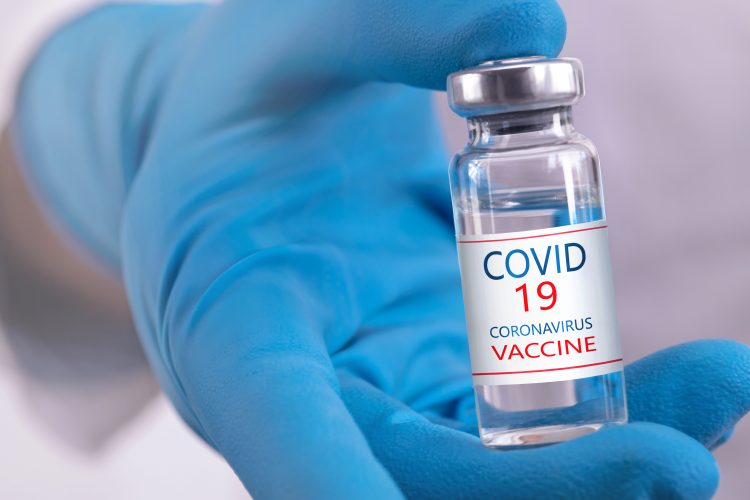 vial in blue gloved hand labelled 'COVID 19 Coronavirus Vaccine'