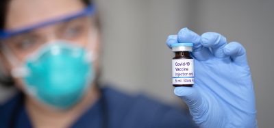 doctor in a mask holding a vial labelled 'COVID-19 Vaccine'