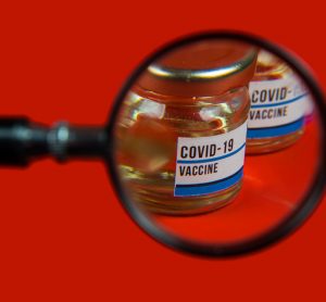 Vial labelled 'COVID-19 Vaccine' under a magnifying glass - idea of vaccine safety/pharmacovigilance