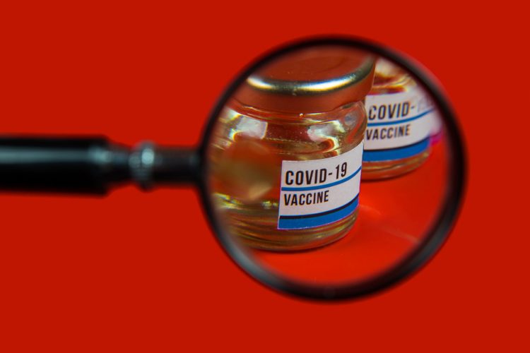 Vial labelled 'COVID-19 Vaccine' under a magnifying glass - idea of vaccine safety/pharmacovigilance