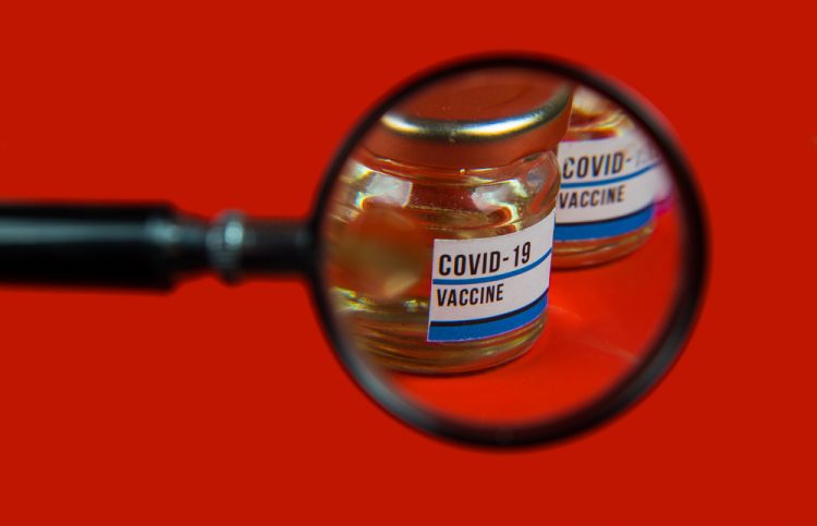 Vial labelled 'COVID-19 Vaccine' under a magnifying glass - idea of vaccine safety/pharmacovigilance