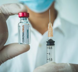 Doctor holding up a syringe and a vial labelled 'CORONAVIRUS VACCINE'