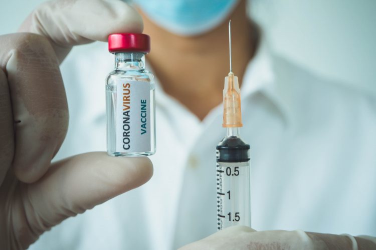 Doctor holding up a syringe and a vial labelled 'CORONAVIRUS VACCINE'