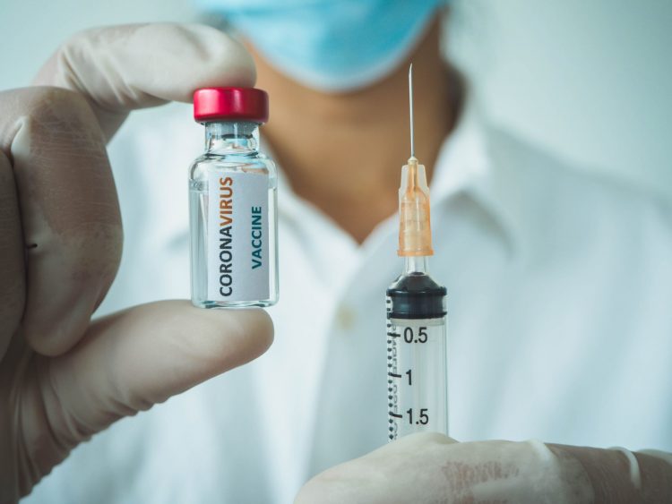 Doctor holding up a syringe and a vial labelled 'CORONAVIRUS VACCINE'