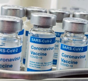 Vials labelled 'COVID-19 CORONAVIRUS VACCINE' lined up on a metal work surface