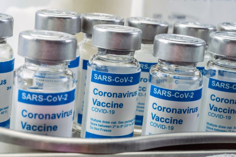 Vials labelled 'COVID-19 CORONAVIRUS VACCINE' lined up on a metal work surface