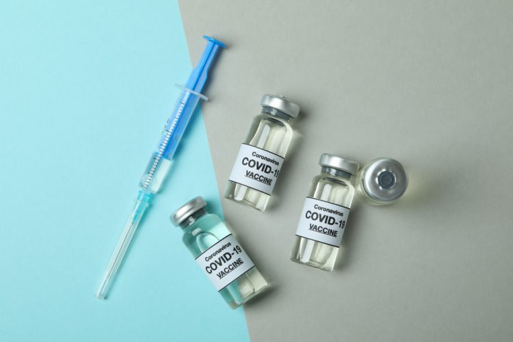 4 Vials labelled 'COVID-19 Vaccine' next to a syringe