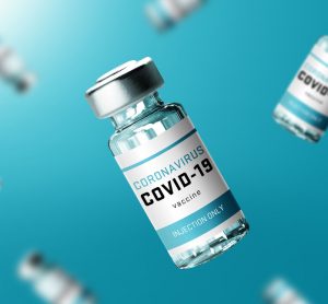 Glass vials labelled 'COVID-19 CORONAVIRUS VACCINE' falling in front of a turquoise background'