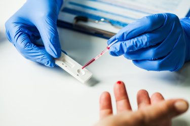 Person with pricked finger having their blood pipetted into a COVID-19 antigen rapid diagnostic test. Antigen rapid diagnostic tests enable front-line healthcare workers to test whether a patient has COVID-19 at the point-of-care with results available in minutes.