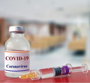 vial of liquid labelled 'COVID-19 coronavirus' with a syringe on a blurred background