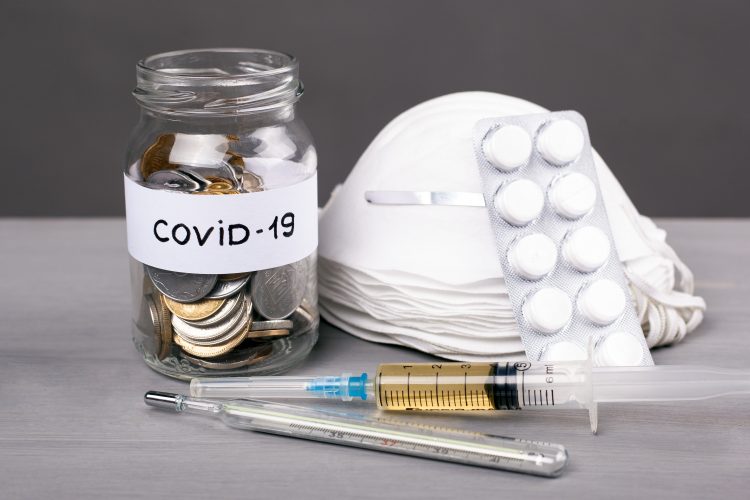 a pile of face masks next to a syringe, a thermometer and a jar of coins labelled 'COVID-19'