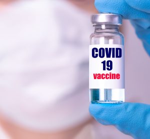 doctor wearing face mask holding a vial labelled 'COVID-19 Vaccine'