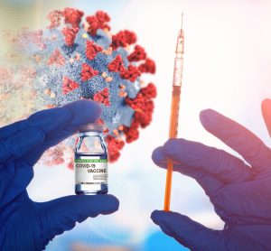 Disintegrating black and red coronavirus particle overlaid with gloved hands holding a vial labelled 'COVID-19 VACCINE' and a syringe