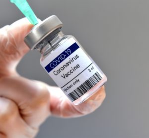 Vial labelled 'COVID-19 CORONAVIRUS VACCINE' with syringe drawing from it