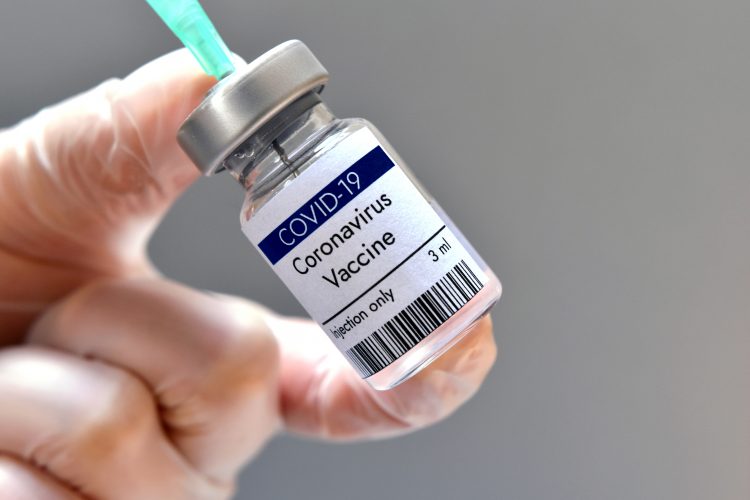 Vial labelled 'COVID-19 CORONAVIRUS VACCINE' with syringe drawing from it