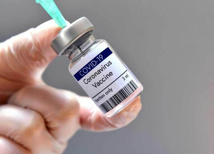 Vial labelled 'COVID-19 CORONAVIRUS VACCINE' with syringe drawing from it