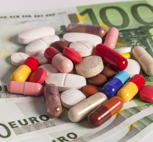 Various colours/sizes/shapes of pills and capsules laid out on a stack of 100 Euro notes