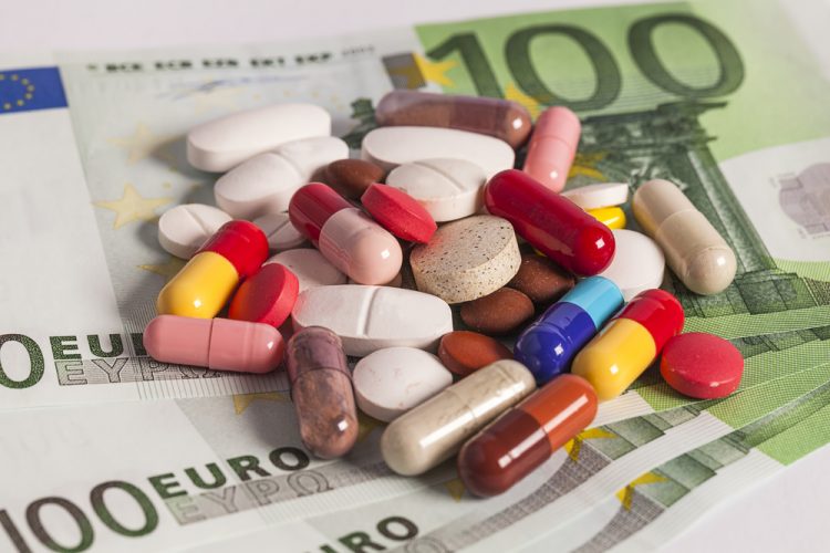 Various colours/sizes/shapes of pills and capsules laid out on a stack of 100 Euro notes