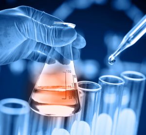 Conical flask containing orange chemical in scientist hand with test tubes behind