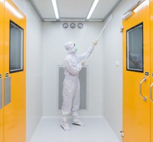 person in cleanroom garments cleaning the walls of a sterile facility with a tool