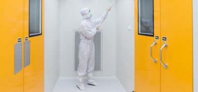 person in cleanroom garments cleaning the walls of a sterile facility with a tool