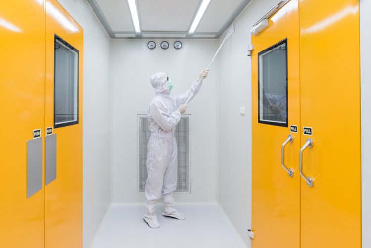 person in cleanroom garments cleaning the walls of a sterile facility with a tool