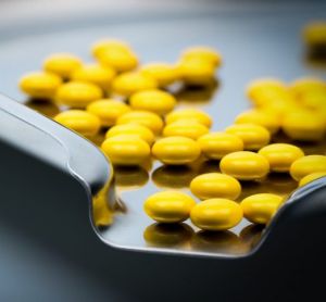 Yellow round sugar coated tablets pills on stainless steel tray.