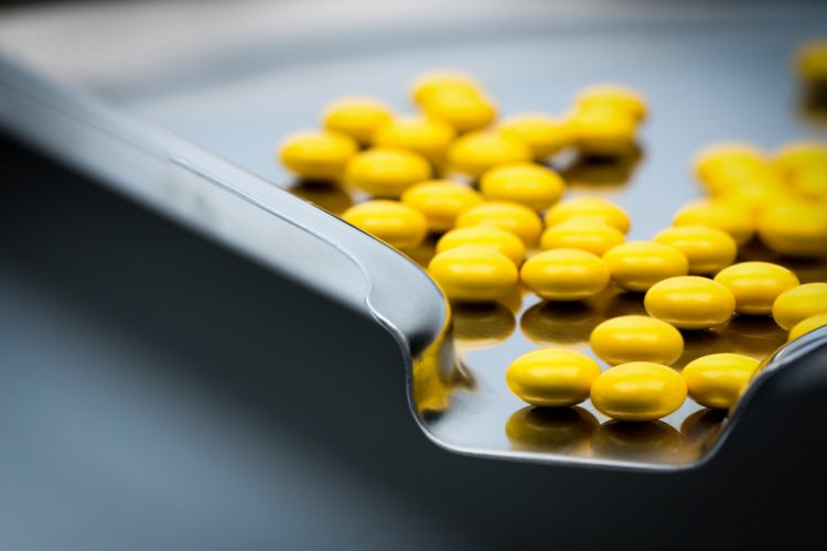 Yellow round sugar coated tablets pills on stainless steel tray.