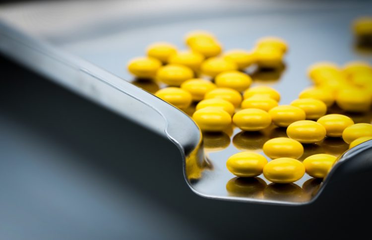 Yellow round sugar coated tablets pills on stainless steel tray.