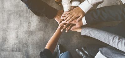 close up of the hands of a group of business people piled together in the middle of a circle - idea of collaboration