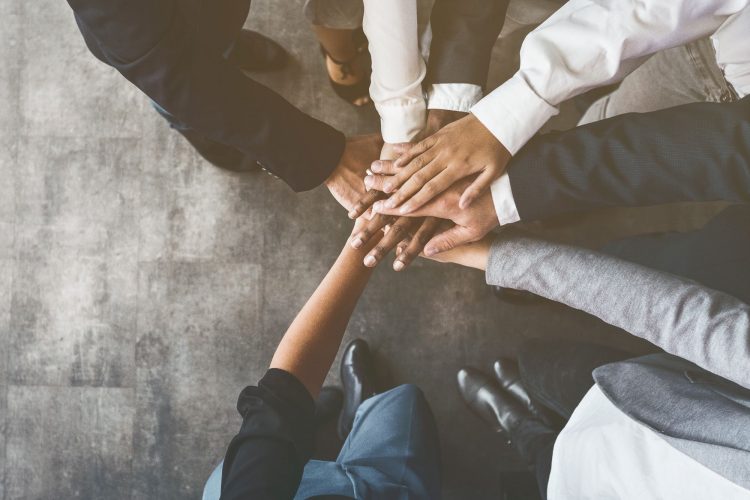 close up of the hands of a group of business people piled together in the middle of a circle - idea of collaboration