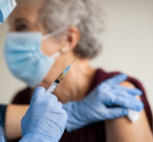 Close up of general practitioner hand holding vaccine injection while wearing face protective mask during covid-19 pandemic.