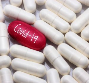 White tablets surrounding a red one labelled COVID-19 - idea of COVID-19 treatment