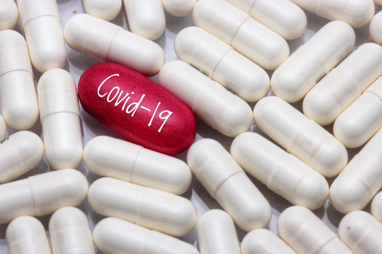 White tablets surrounding a red one labelled COVID-19 - idea of COVID-19 treatment