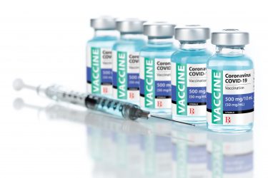 Five vials lined up labelled 'COVID-19 CORONAVIRUS VACCINE' next to a syringe